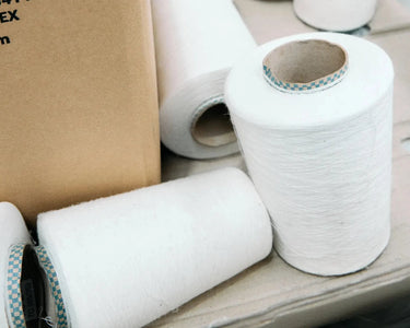 Spools of white fabric on a cardboard box with visible text.
