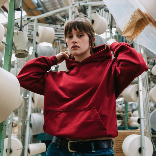 Person wearing a red hoodie in an industrial setting with large spools of thread.