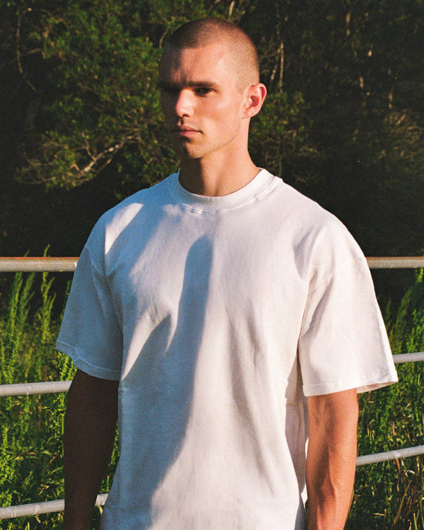 Man wearing a plain white t-shirt standing outdoors with trees in the background